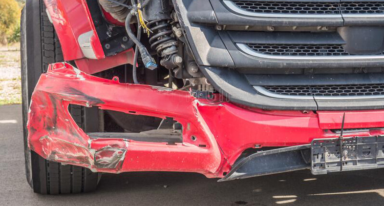 A professional assesses a damaged truck's front end, documenting the extent of the crash for truck accidental and body repairing services.