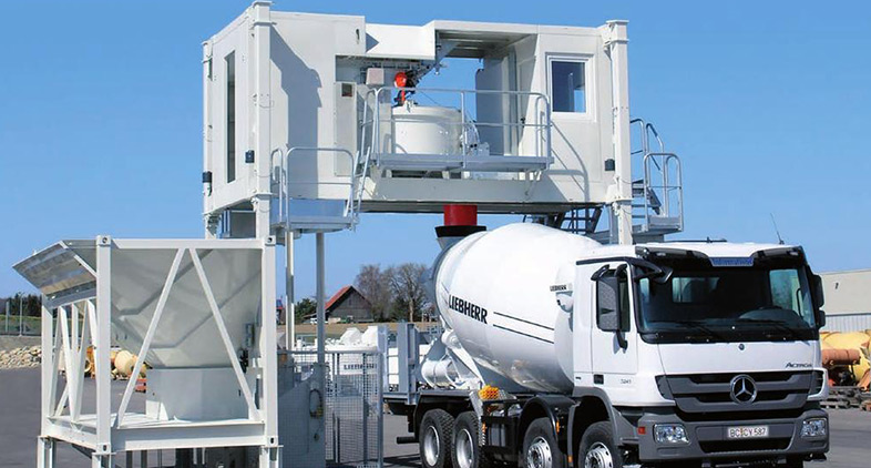 A Liebherr concrete mixer truck being loaded at a mobile batching plant, illustrating the process of batching plant repairs & service for construction operations.