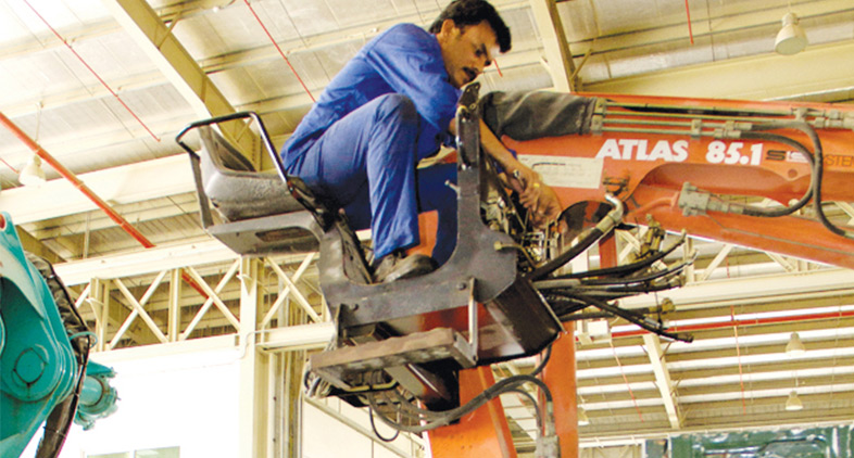 A skilled technician works on the hydraulic system of an Atlas crane boom, providing repairs and service for cranes and excavators in a workshop environment.