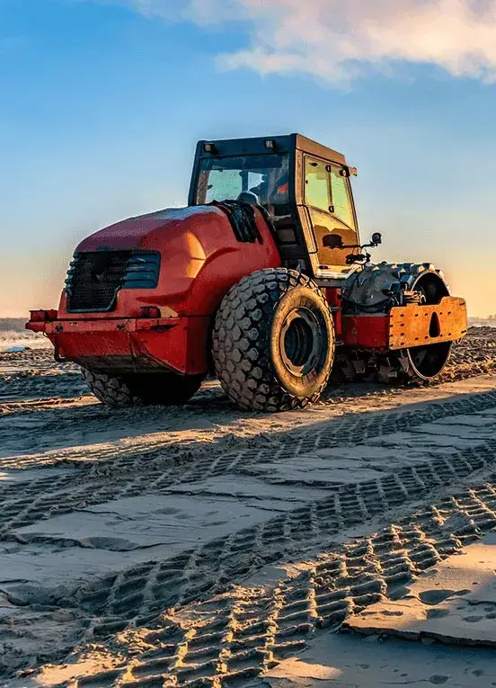 An orange construction equipment roller, showcasing heavy machinery, makes tracks in the sand. Ideal for construction equipment UAE, heavy equipment movers, construction equipment companies, and heavy equipment and machinery suppliers.